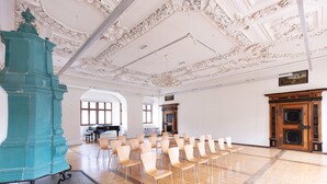 A spacious hall with rows of chairs, a large teal pillar, and ornate ceiling details.