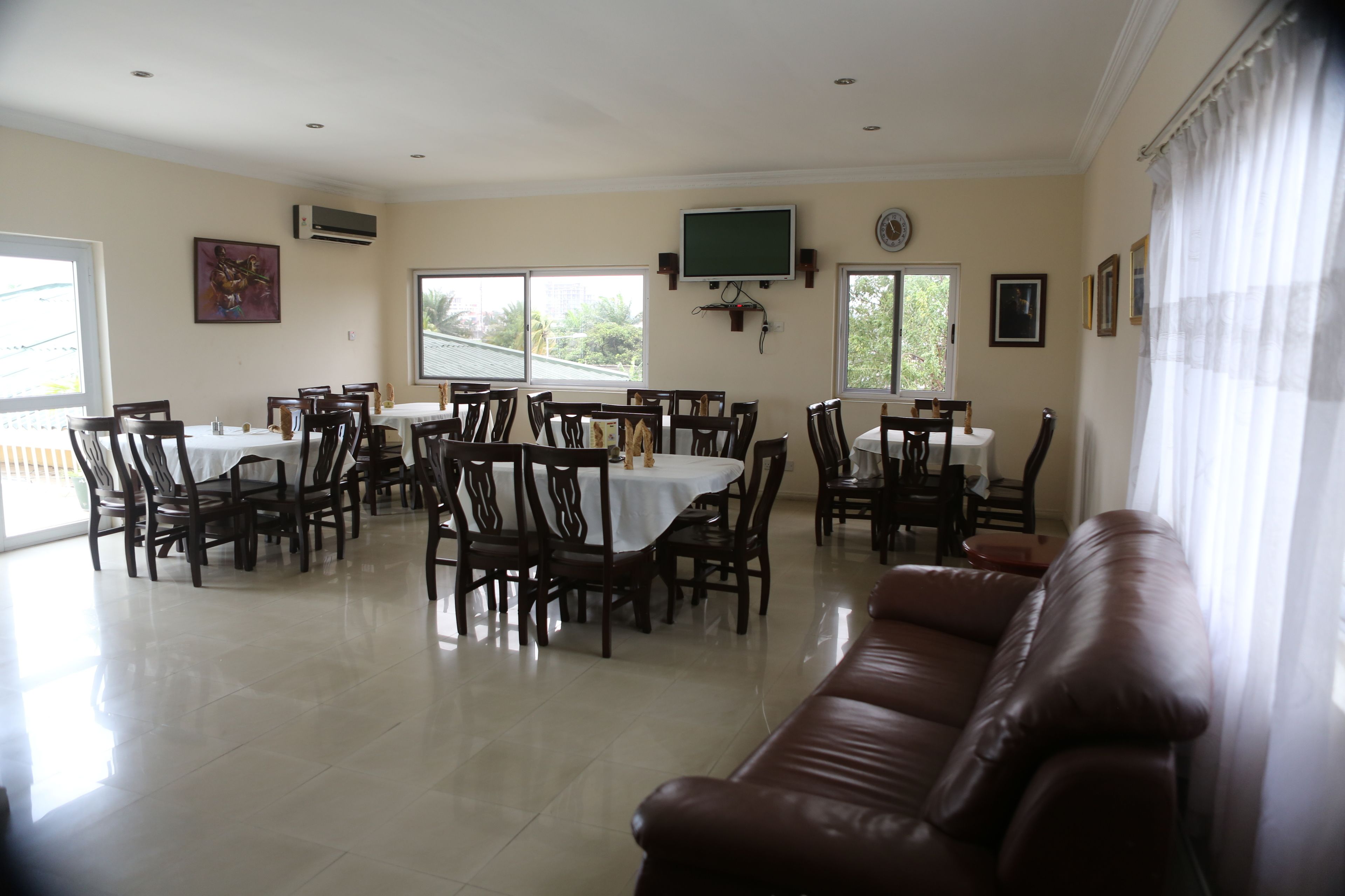 A dining area with multiple tables and chairs, a television mounted on the wall, and a large window providing natural light.
