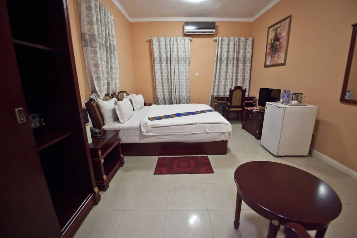A hotel room with a bed, a desk, a chair, a wardrobe, and an air conditioning unit.