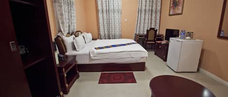 A hotel room with a bed, a desk, a chair, a wardrobe, and an air conditioning unit.