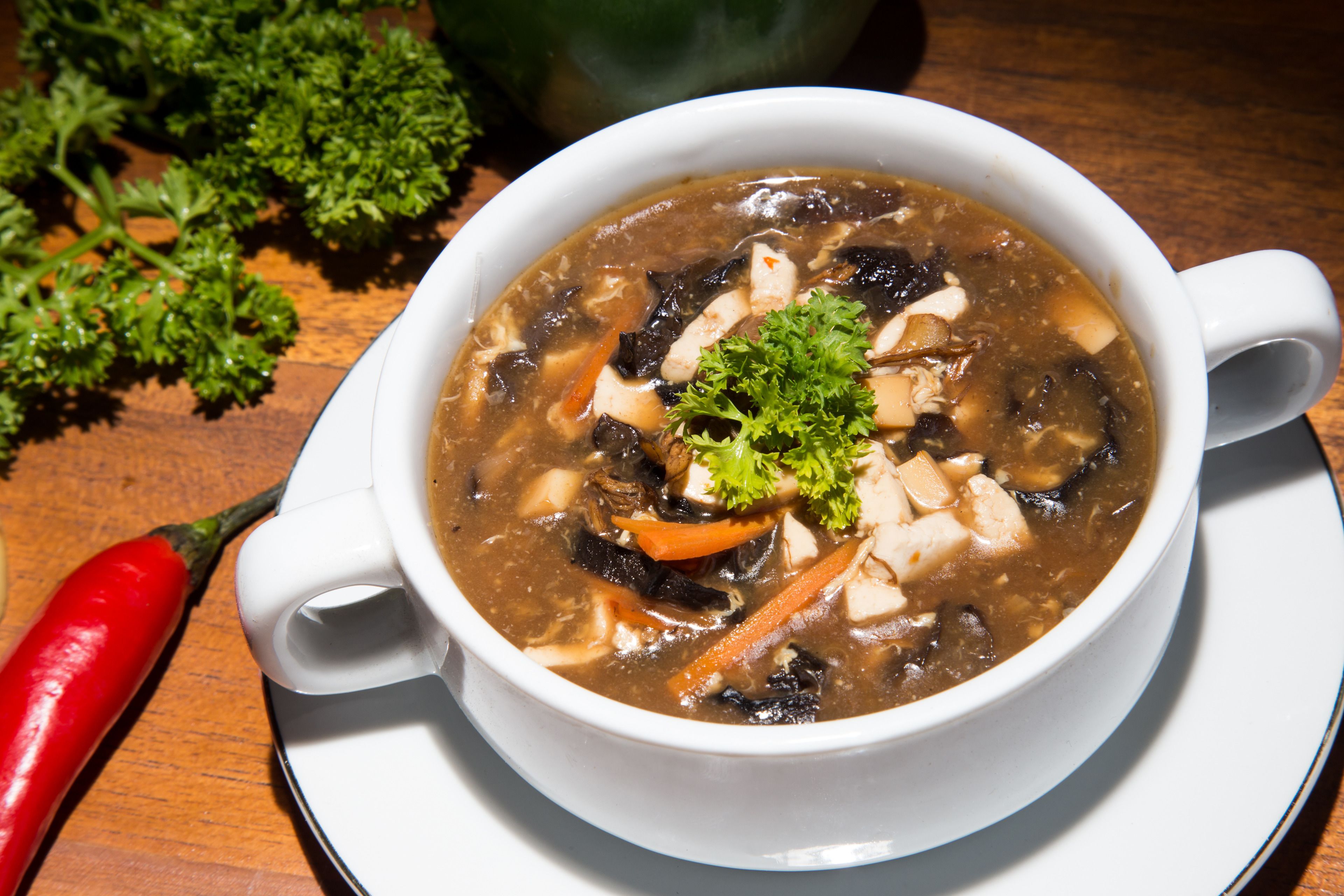 A bowl of soup with vegetables and tofu on a wooden table.