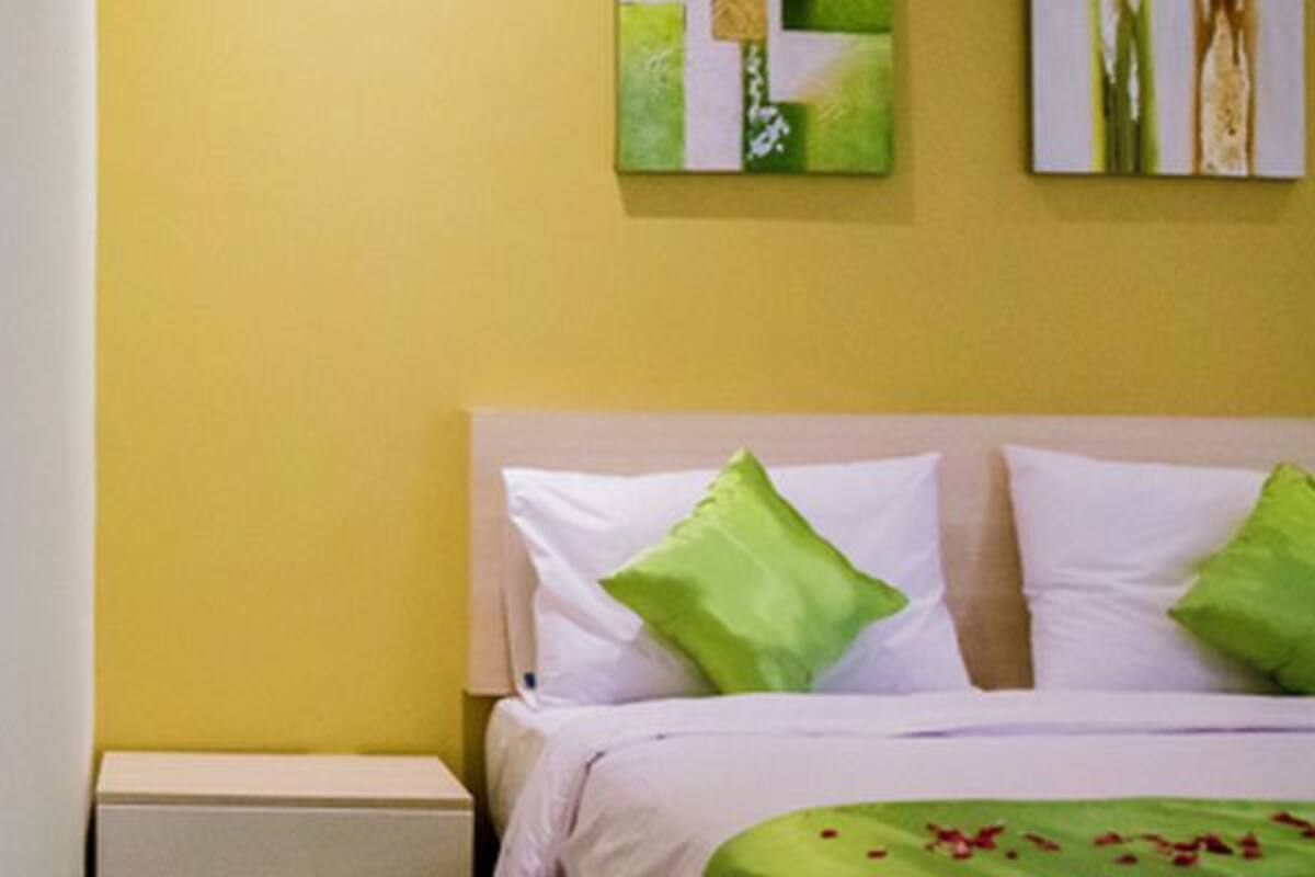 A hotel room with a bed, a nightstand, a bedside table, a glass shower enclosure, and a bathroom with a sink and mirror.