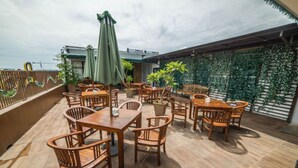 An outdoor patio with wooden tables and chairs, green umbrellas, and potted plants. - Best Inn Hotel (Balikpapan)