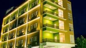A multi-story building with balconies, illuminated windows, and a street with green lights. - Best Inn Hotel (Balikpapan)