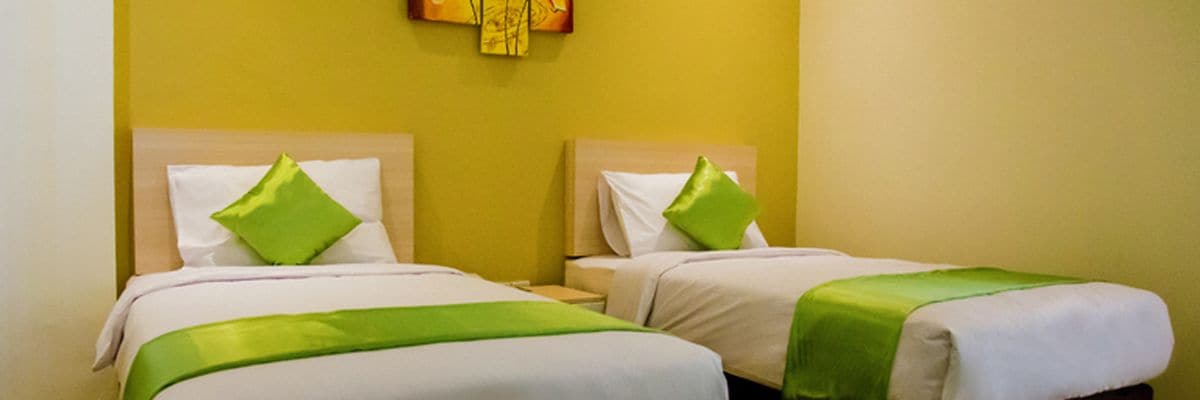 Two twin beds with green pillows and a green blanket, in a room with yellow walls.