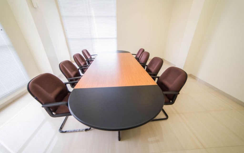 Een vergaderruimte met een lange tafel en acht bruine stoelen.