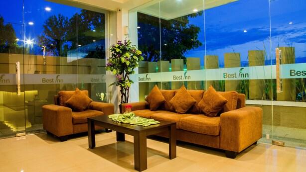 A modern hotel lobby with two sofas and a coffee table, large windows, and a view of trees. - Best Inn Hotel (Balikpapan)