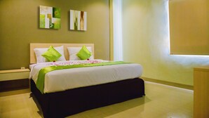 A neatly made bed with green and white bedding, a nightstand, and two wall art pieces. - Best Inn Hotel (Balikpapan)