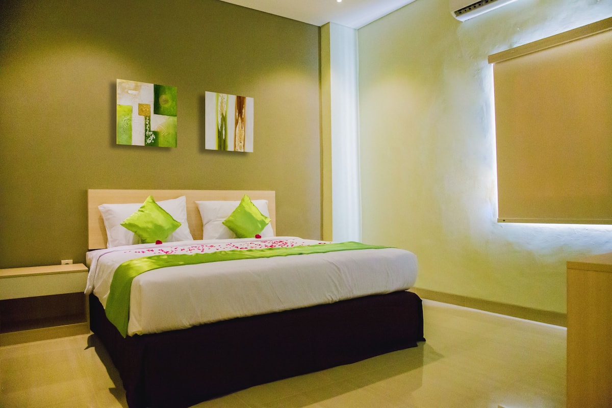 A neatly made bed with green and white bedding, a nightstand, and two wall art pieces.