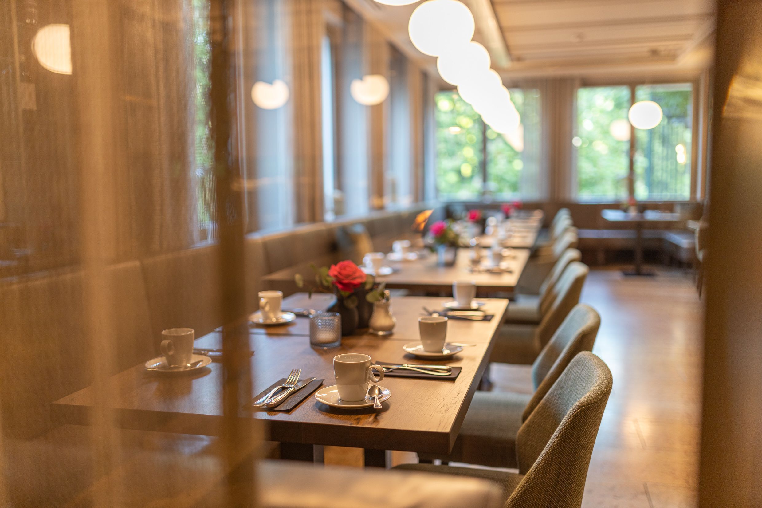 A restaurant with long tables, chairs, and a vase with flowers.