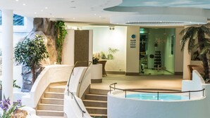 A hotel lobby with a pool, stairs, and indoor plants. - Parkhotel Schmid (Adelsried)