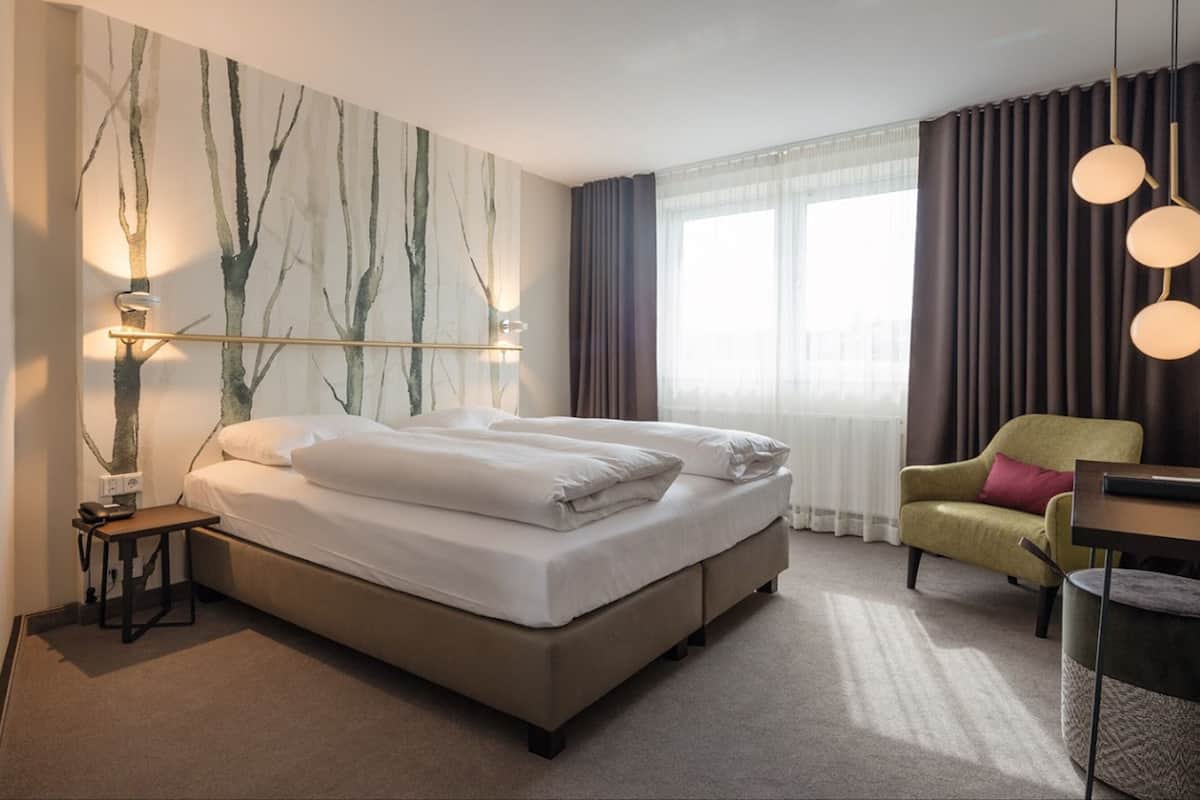 Quarto de hotel com uma cama grande, uma escrivaninha, uma cadeira e uma janela com cortinas.