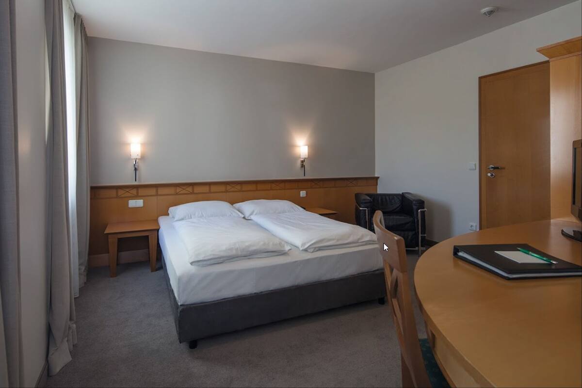 Quarto de hotel com cama de casal, mesas de cabeceira, escrivaninha e uma cadeira, e porta.