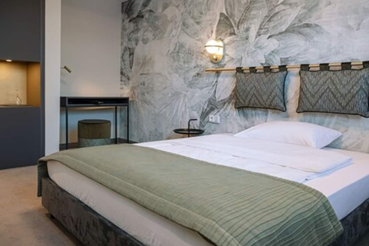 Quarto moderno com parede com padrão marmorizado, cama com colcha verde e luminária fixada na parede.