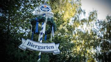 Letrero con el texto 'Biergarten' y 'Schneider Weisse', rodeado de follaje.