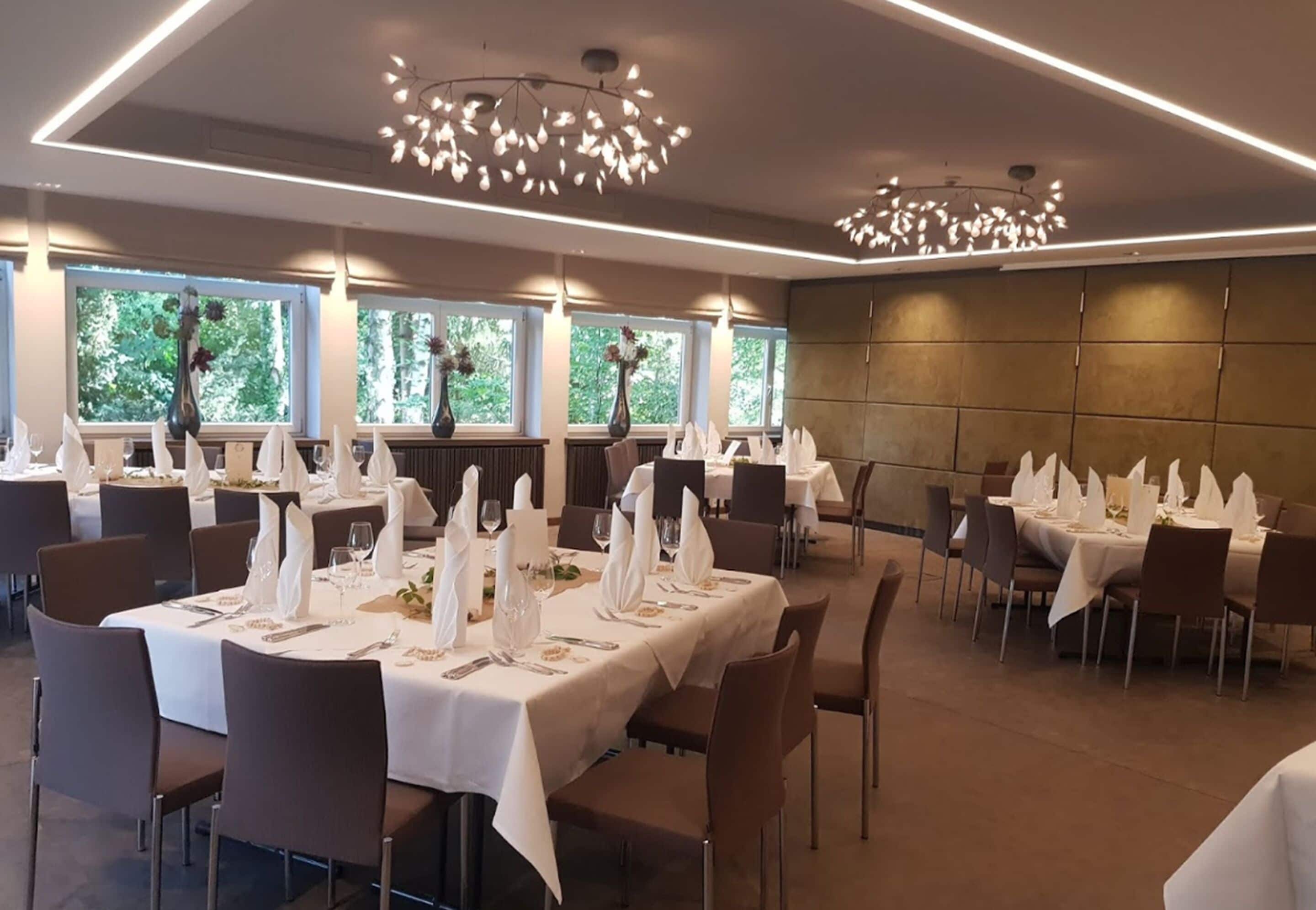 Comedor con mesas dispuestas para el servicio, ventanas amplias y luminarias modernas.