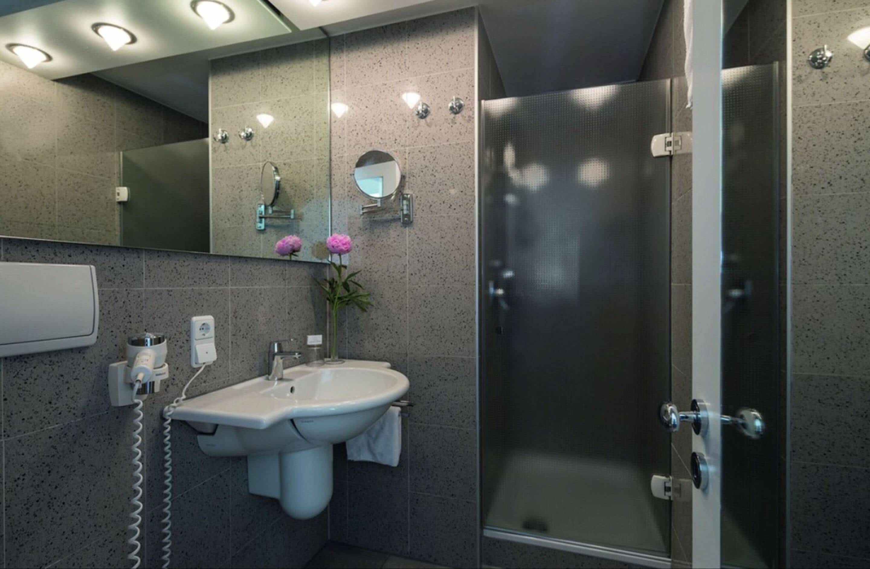 Un baño moderno con ducha envuelta en vidrio, un lavabo blanco con una toalla y un espejo encima.