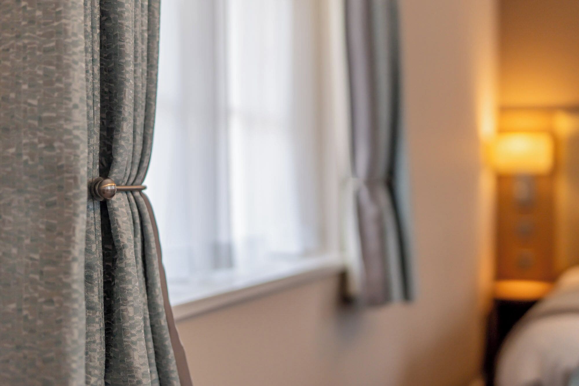A close-up of a window with curtains tied back, revealing a blurred interior room.