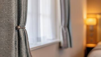 A close-up of a window with curtains tied back, revealing a blurred interior room.