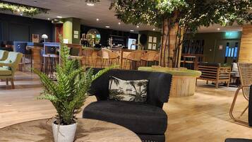 A modern lounge area with a round wooden table, black sofas, and wicker chairs.