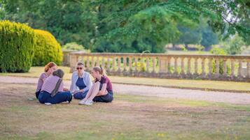 A group of people sitting on the grass in a park with a stone balustrade in the background.