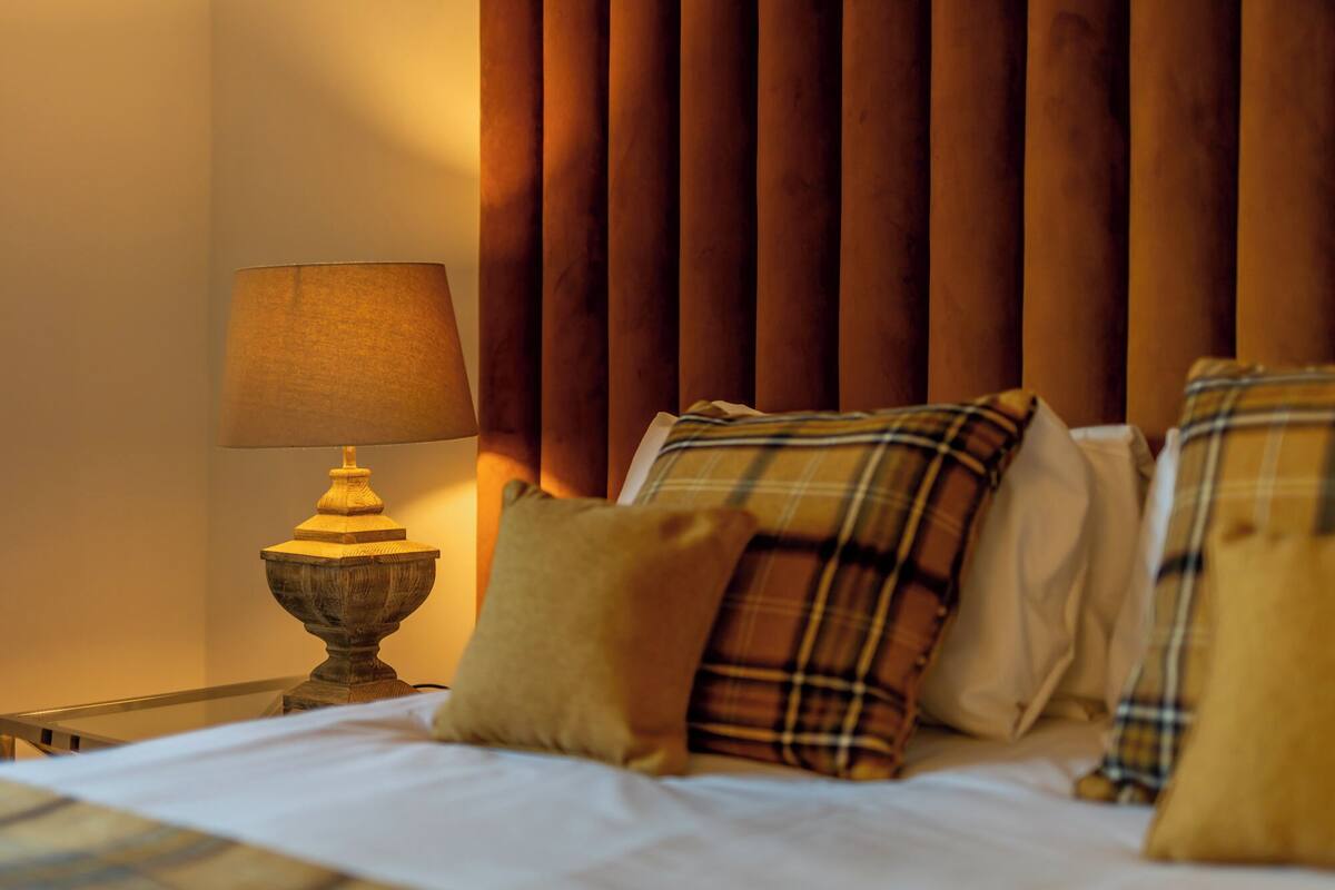 A bed with plaid pillows, a wooden headboard, and a table lamp.