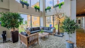 A spacious indoor area with a large window, a sofa set, a coffee table, and several potted plants. - Ashorne Hill Leamington Spa (Royal Leamington Spa)