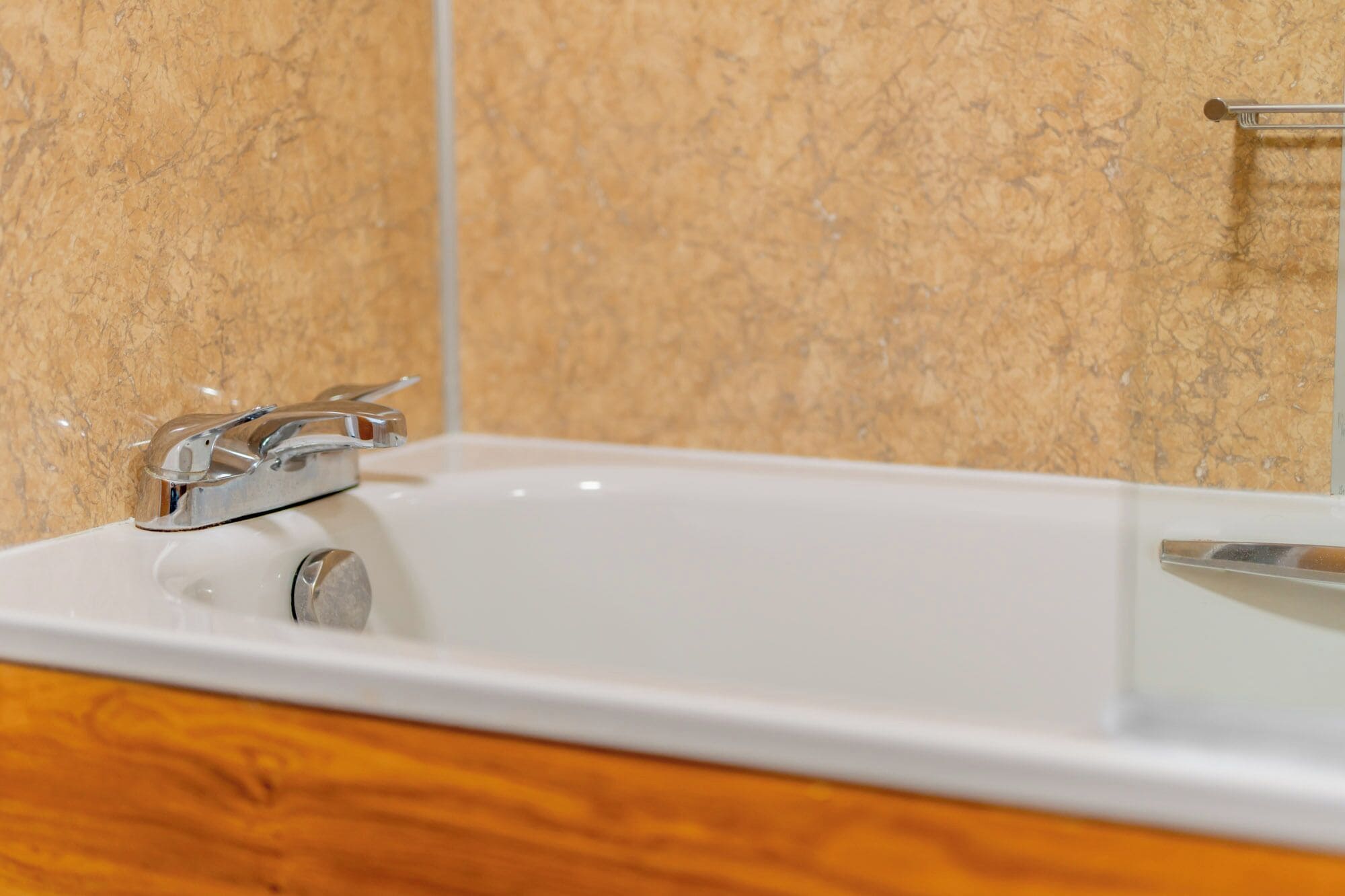 A bathroom with a white bathtub, chrome faucet, and wooden vanity.