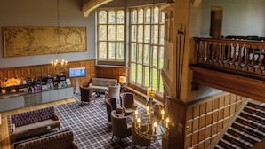 A spacious lobby with a checkered floor, a bar area with a television, and a staircase with a wooden railing. - Ashorne Hill Leamington Spa (Royal Leamington Spa)