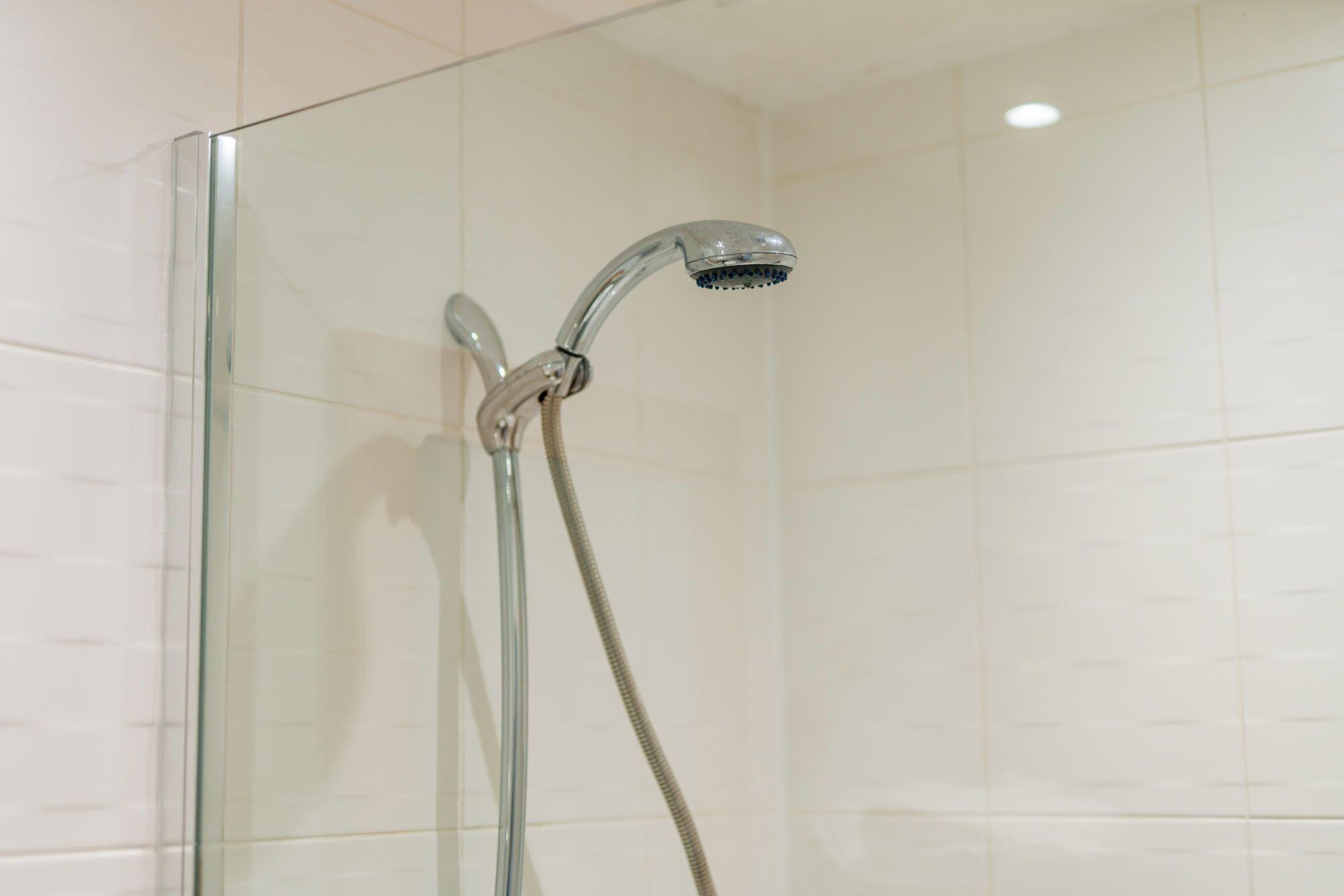 Une douche fermée par des parois en verre, dotée d’un pommeau et d’un flexible chromés.