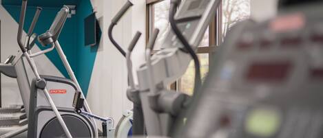 An exercise machine with a digital display, a wall-mounted air conditioning unit, and a window with a view of trees.