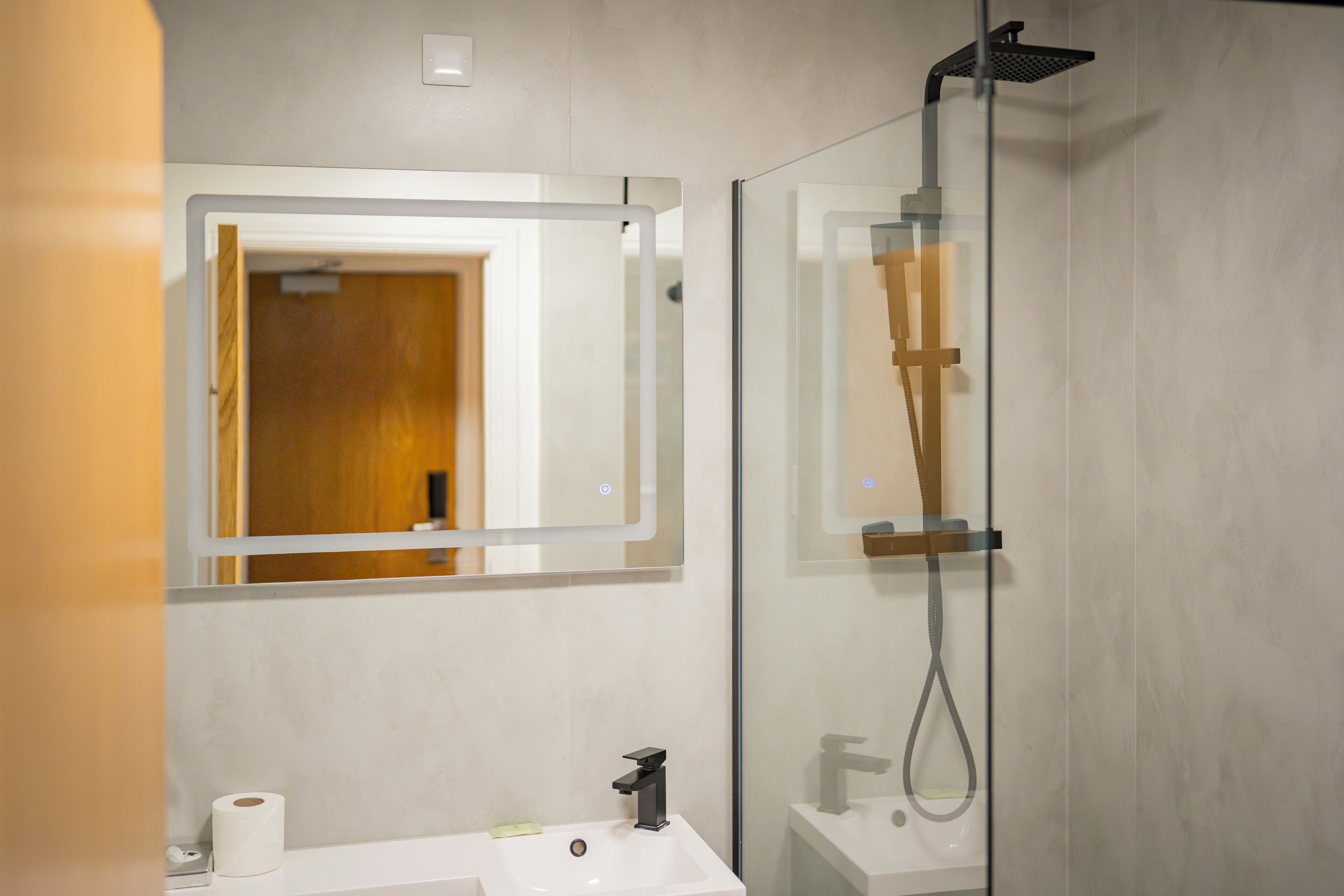 Ein modernes Badezimmer mit Duschkabine aus Glas, einem weißen Waschbecken und einem Spiegel mit Holzrahmen.