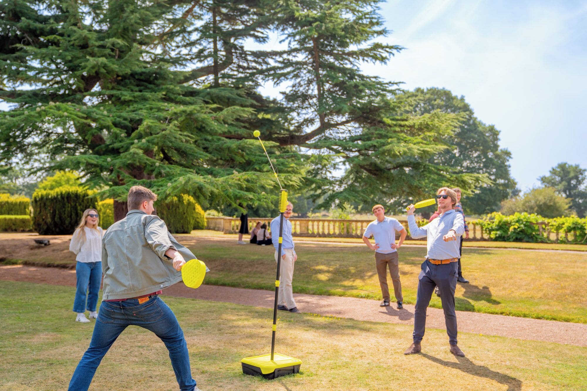 A group of people playing a game outdoors in a park with trees and a clear sky.
