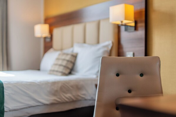 A hotel room with a bed, pillows, and a chair. There are two wall-mounted lamps on either side of the bed.