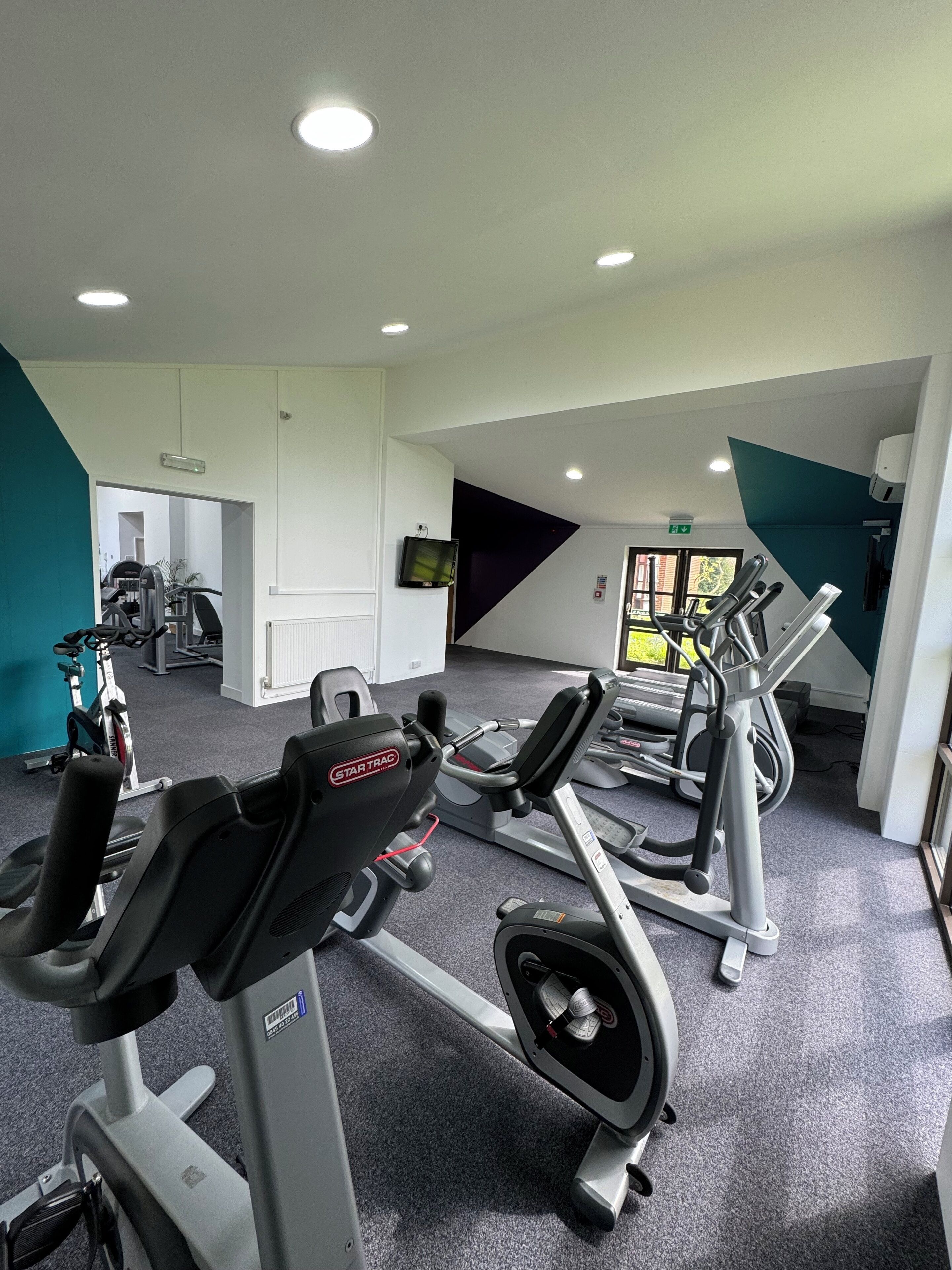 A gym with various exercise equipment, including treadmills and weight machines, and a large mirror on the wall.