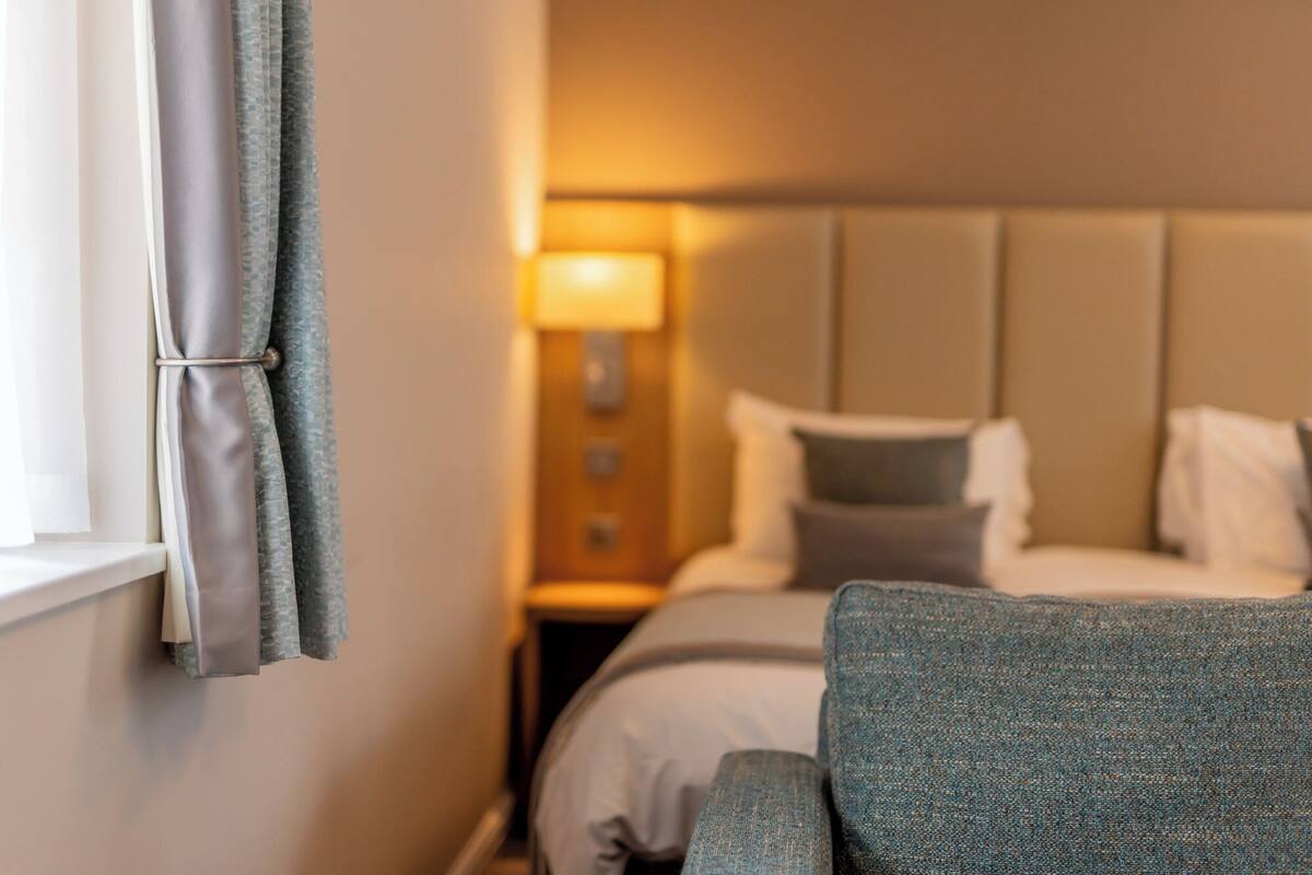 A hotel room with a bed, a nightstand, a lamp, and a chair.