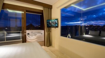 Quarto de hotel moderno com uma cama grande, hidromassagem, televisão e varanda com vista noturna.