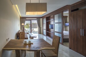 Quarto de hotel moderno com uma mesa de jantar de madeira, cadeiras, um sofá e uma televisão.