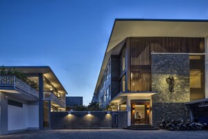 Um hotel moderno com fachada de pedra, uma varanda e área de estacionamento com motociclos.