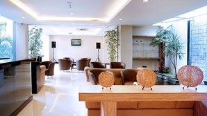 A modern hotel lobby with a reception desk, seating area, and a small indoor garden.