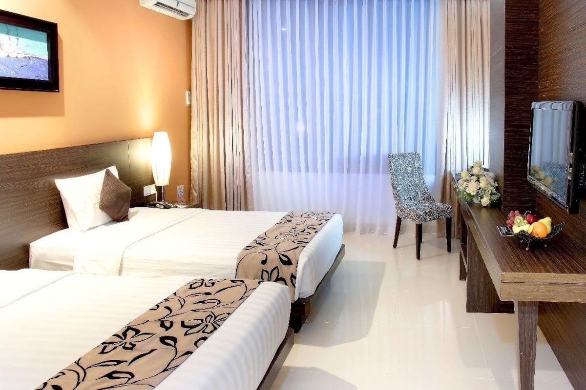 A hotel room with two beds, a desk with a vase of flowers, and a television on the wall.