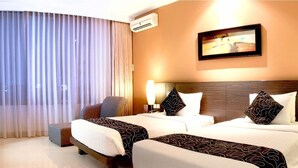 A hotel room with two beds, a desk with a chair, a TV, and a large window with curtains.
