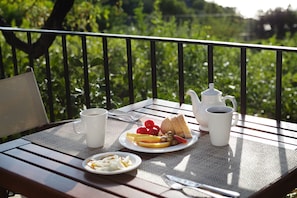 Una mesa dispuesta con alimentos para el desayuno, como tostadas, fruta y café, con vistas a follaje en el fondo.