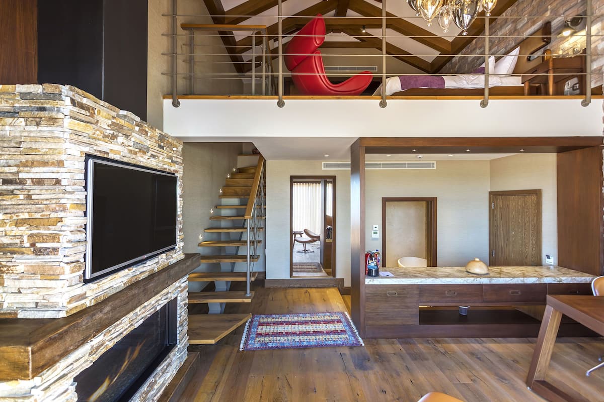 Een modern loft met een stenen open haard, een grote televisie, een houten trap en een rode sculptuur.