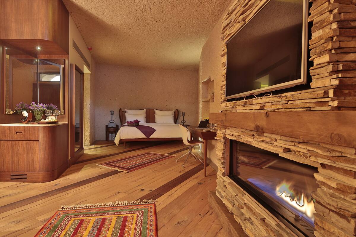 Een slaapkamer met een bed, een houten dressoir, een open haard en een grote televisie bevestigd aan een stenen muur.