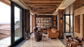 A spacious living area with a large window, a leather sofa, a wooden coffee table, and a fireplace. - Ariana Sustainable Luxury Lodge - Special Class (Nevsehir)