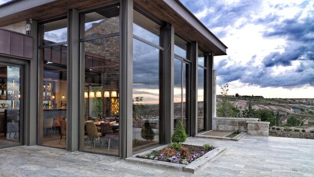 A modern building with large glass windows, a stone facade, and a patio area with plants. - Ariana Sustainable Luxury Lodge - Special Class (Nevsehir)