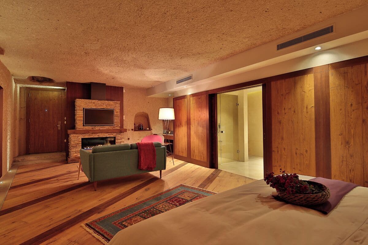 Een moderne hotelkamer met een stenen openhaard, een groene bank, een groot bed en een houten vloer.