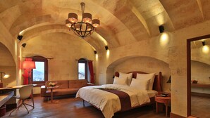 A bedroom with a wooden bed, a desk, and a chair. There is a chandelier above the bed and a window with curtains. - Ariana Sustainable Luxury Lodge - Special Class (Nevsehir)