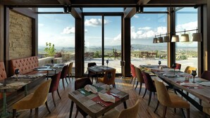 A restaurant with a high ceiling, exposed beams, and large windows offering a scenic view of the countryside. Tables are set with white tablecloths and red placemats. - Ariana Sustainable Luxury Lodge - Special Class (Nevsehir)